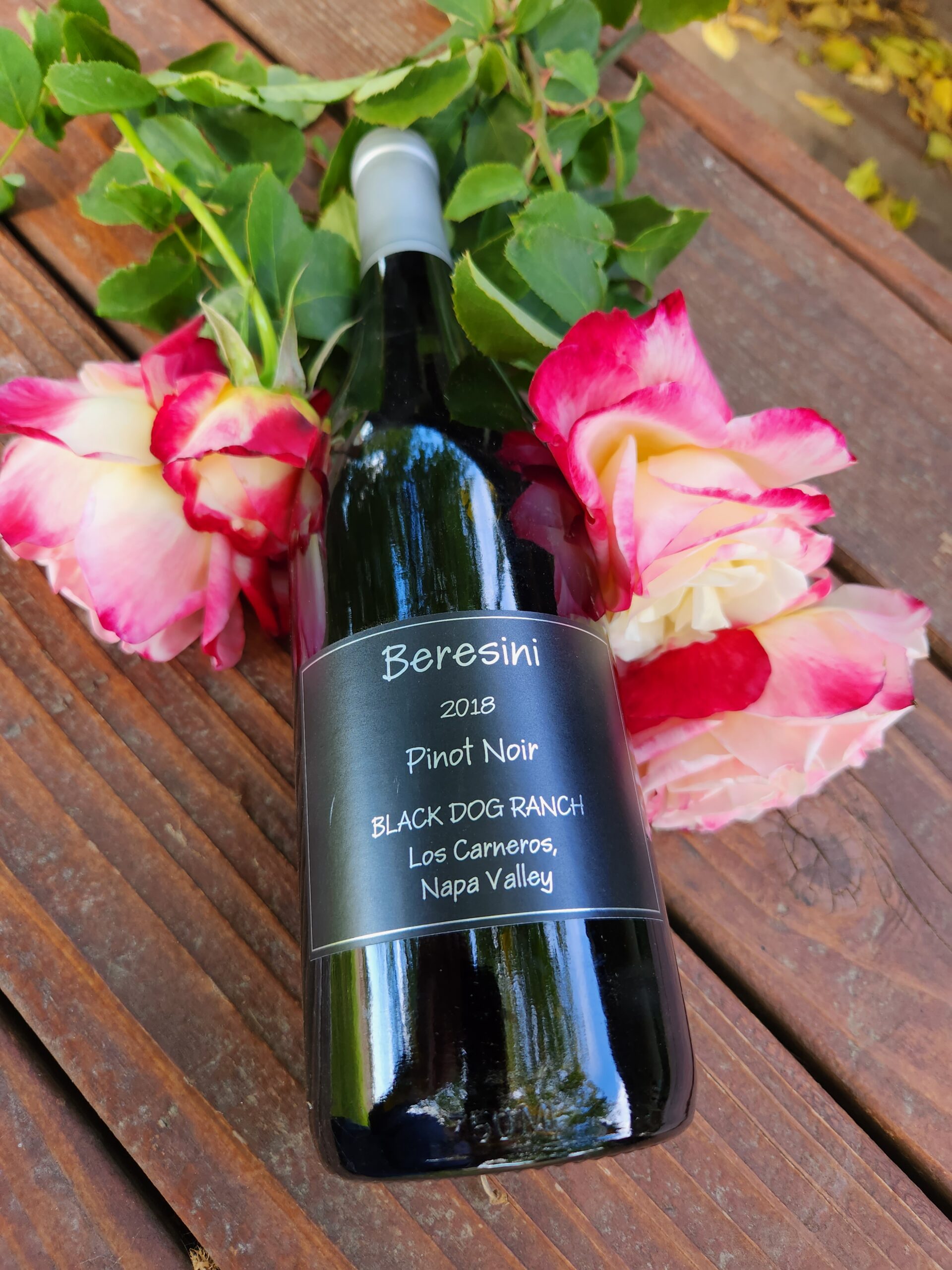 Bottle of 2018 Pinot Noir on a picnic table with flowers